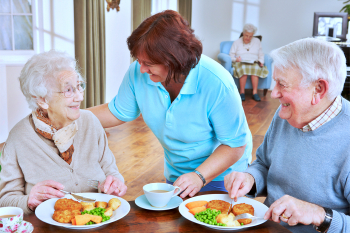 caregiver assists the two seniors in eating